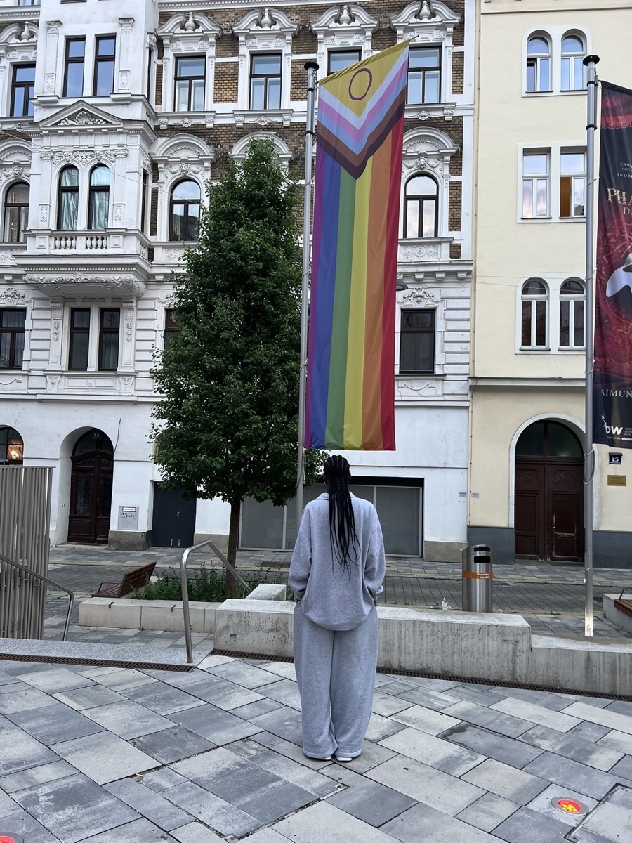 A person standing before a progress Pride flag on a city street